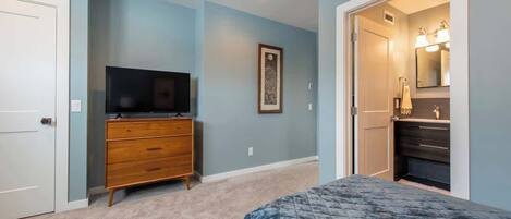 Une chambre à coucher comprenant un lit, une commode, un téléviseur et une salle de bain avec un miroir et un lavabo.