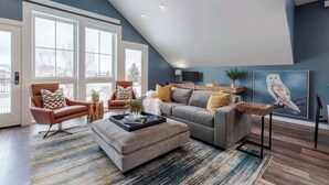 A modern living room with a sloped ceiling, large windows, a grey sofa, two armchairs, and a coffee table.