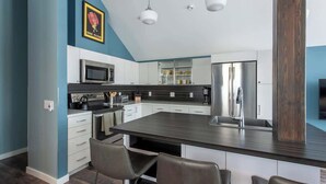 A modern kitchen with a central island, white cabinets, stainless steel appliances, and pendant lighting.