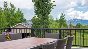 A balcony with a table and chairs, a view of a mountain, and a house in the background.
