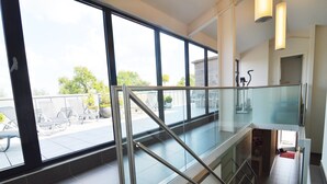 Un interior moderno con barandilla de vidrio, una escalera y vistas a un área de estar al aire libre.