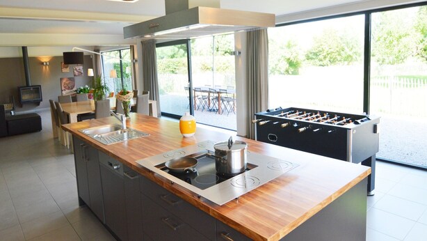 Una cocina moderna con una isla central, estufa integrada y una mesa de futbolín.
