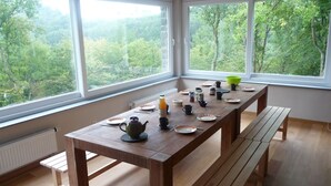 A wooden dining table with plates, cups, and a teapot, set against a window overlooking a forested area. - Eco Hilltop Home in Falaën (Falaën)