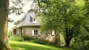 A stone house with a sloped roof, surrounded by lush greenery and trees. - Eco Hilltop Home in Falaën (Falaën)