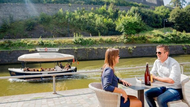 A boat named "NAMOURETTE" on a river, a couple dining at a table with a bottle of wine, and a stone wall in the background. - Eco Hilltop Home in Falaën (Falaën)