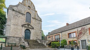 A historic stone building with a large arched window and a door, a staircase leading to the entrance, and a paved courtyard. - Scenic Retreat in Gimnée (Gimnée)