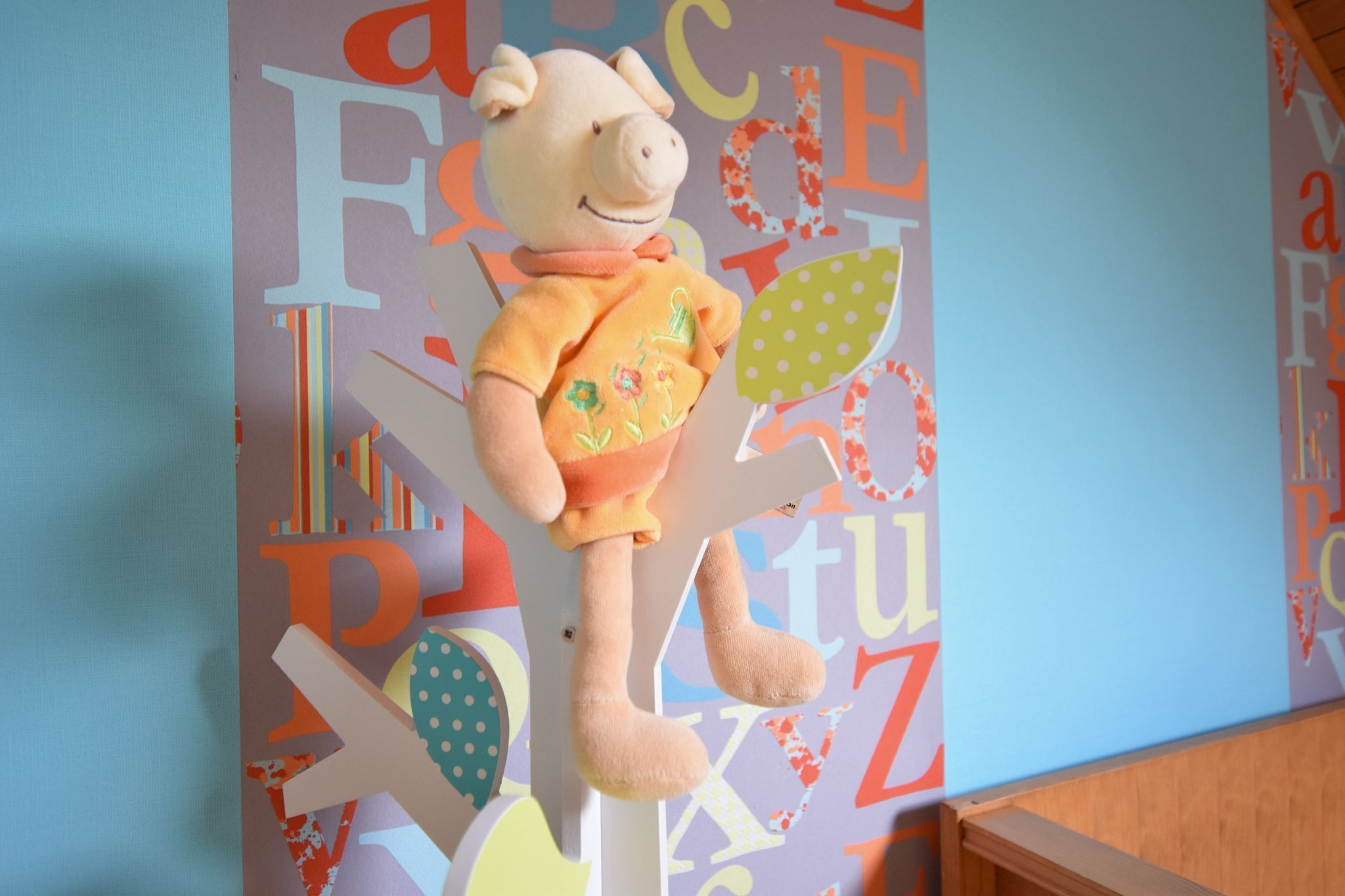 A plush toy pig on a white stand against a wall with colorful letters.
