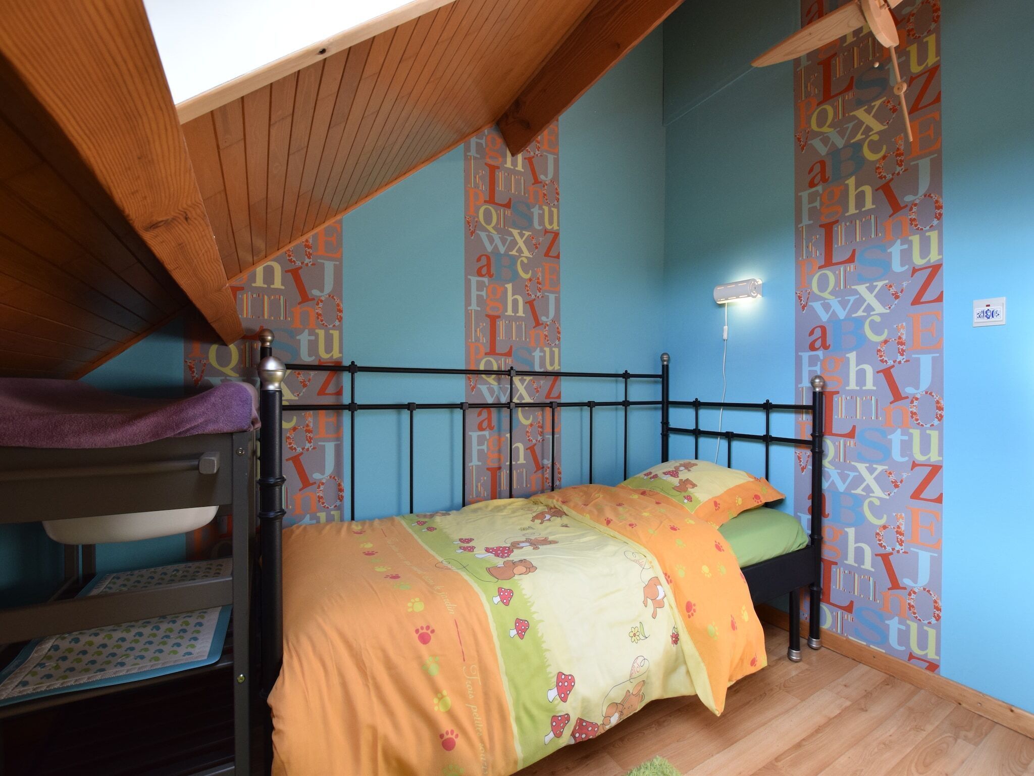 A dormitory room with bunk beds, a ceiling fan, and alphabet-themed wallpaper.