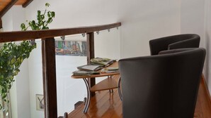 A room with a wooden ceiling, a balcony with a view of a cityscape, a table with books and papers, and a chair. - Nature Escape in Martelange (Martelange (radelange))