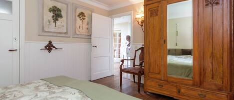 A bedroom with a large wooden wardrobe, a bed with a patterned bedspread, and a wall-mounted mirror.
