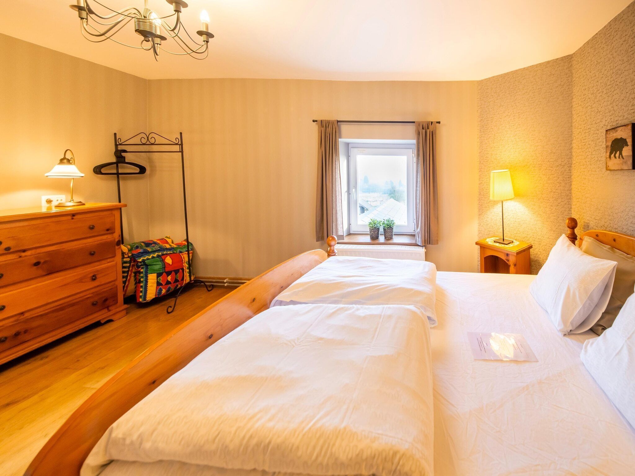 Une chambre d’hôtel avec un grand lit, une commode en bois et un lustre.