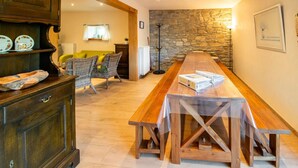 A spacious room with a long wooden table, wicker chairs, a stone wall, and a wooden cabinet with decorative plates. - Charming Home in Ardennes (Petit-Thier)