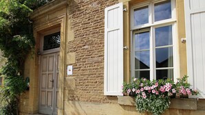 A stone building with a wooden door and white shutters, a set of stone steps, and a flower box with pink flowers. - Rustic Charm, Modern Comfort (Latour)