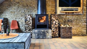 A rustic stone wall with a wood-burning stove, a television mounted above it, and a seating area with a table and chairs.