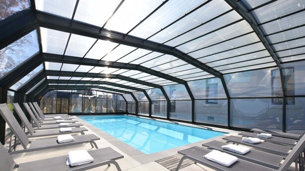 A covered swimming pool with lounge chairs and a glass ceiling.