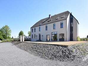 A modern two-story house with a sloped roof, large windows, and a gravel driveway.