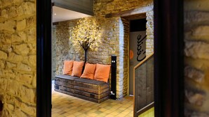 A rustic interior with a stone wall, a wooden ceiling, and a sofa with orange cushions.