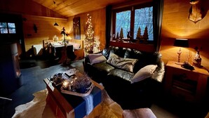 Ein gemütliches Blockhaus-Interieur mit Ledersofa, Esstisch, Weihnachtsbaum und Kamin.