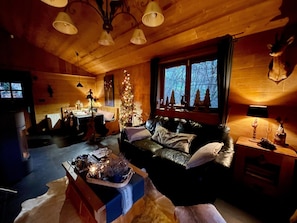 A cozy cabin interior with a leather sofa, a dining table, a Christmas tree, and a fireplace.