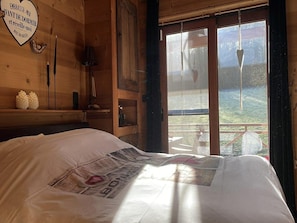 A wooden room with a bed, a window with a view, and a heart-shaped sign on the wall.