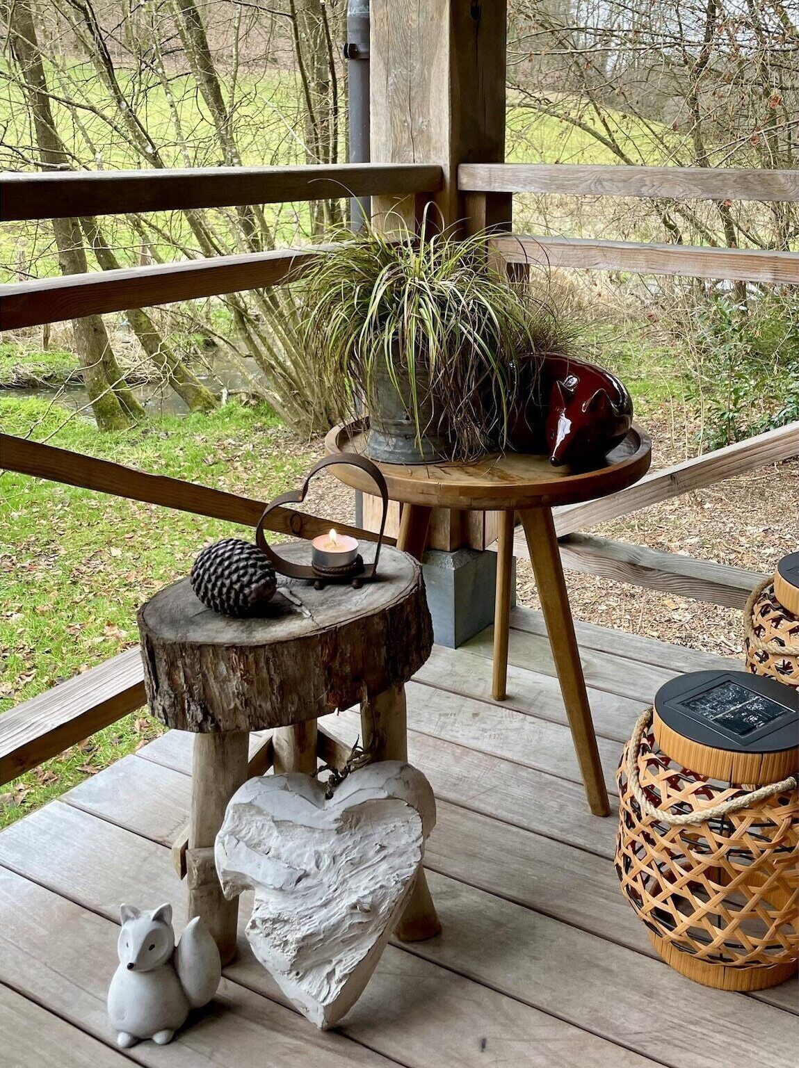 Una terraza de madera con una mesa rústica, una escultura de zorro y una cesta tejida.