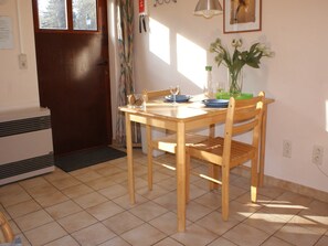Une table à manger en bois, avec des chaises, un vase rempli de fleurs et une fenêtre avec des rideaux.