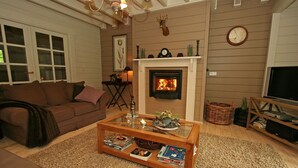 A cozy living room with a fireplace, a sofa, a coffee table with books, and a television on a wooden stand. - Countryside Chalet in 	Bomal sur Ourthe with Sauna, Balcony (Bomal sur Ourthe)