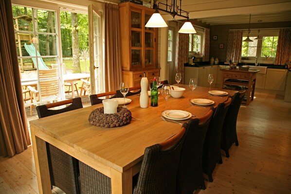 A dining area with a wooden table set for six, surrounded by wicker chairs. A cabinet with glass doors is visible in the background.