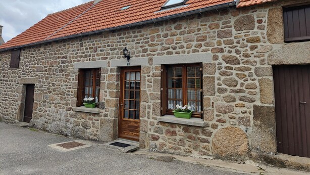 A stone building with a red-tiled roof, wooden doors, and windows with flower boxes.