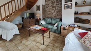 A cozy living room with a wooden staircase, a stone wall, a green and white checkered sofa, a wooden coffee table, and a television on a cabinet.