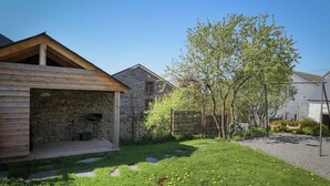 A stone house with a wooden deck, a swing set, and a grassy yard with dandelions.