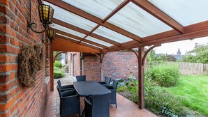 Une terrasse couverte avec un mur en briques, une table avec des chaises et une lanterne.
