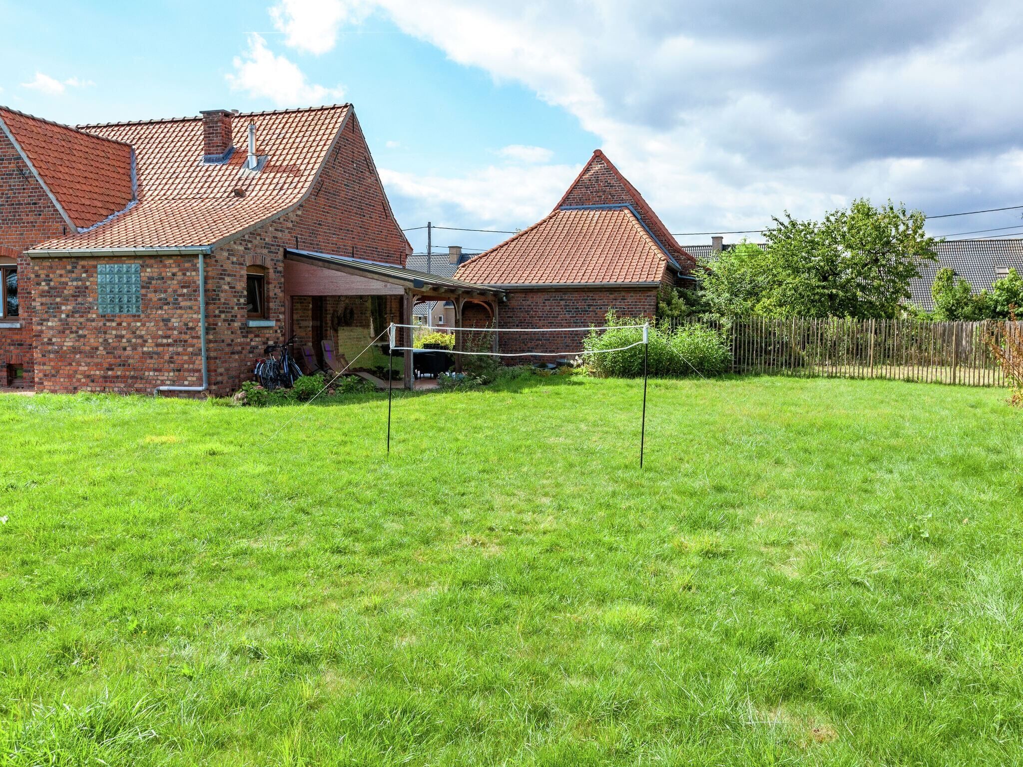 A brick house with a red-tiled roof, a grassy yard, and a volleyball net.
