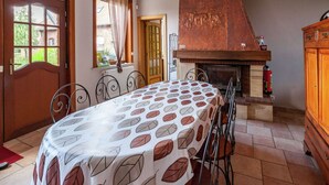 Un coin repas avec une table dressée pour quatre personnes, une cheminée et une vue sur le jardin par la fenêtre.