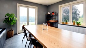 A modern dining room with a wooden table, black chairs, a potted plant, and a built-in shelving unit with plants and decorative items.
