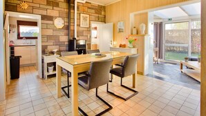 A modern kitchen with a stone backsplash, wooden paneling, and a dining area with a glass table and chairs.