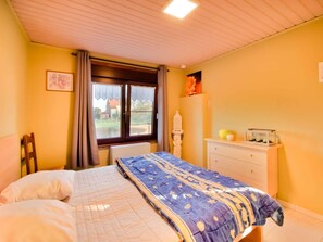 Un dormitorio con cama, cómoda, ventana con cortinas y radiador.