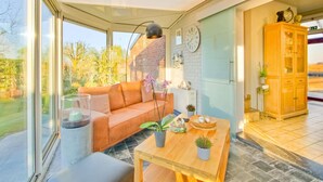 A modern living room with a sofa, a coffee table, and a dining table. There is a large window providing a view of the outdoors.
