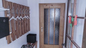 A hallway with a wooden door, a bench with floral cushions, a coat rack with hangers, and a black speaker. - Chalet in Lenk near Simmen Falls (Lenk)
