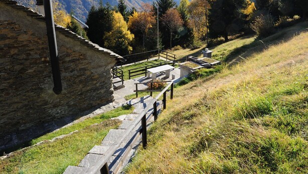 A stone building with a wooden fence, a stone bench, and a paved area with a metal railing. - Chalet in Lenk near Simmen Falls (Lenk)