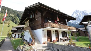 A traditional wooden chalet with a balcony, a staircase leading to the upper floor, and a view of snow-capped mountains in the background. - Chalet in Lenk near Simmen Falls (Lenk)