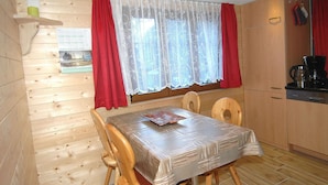 A wooden interior with a dining table, chairs, a kitchen area, and a window with curtains.