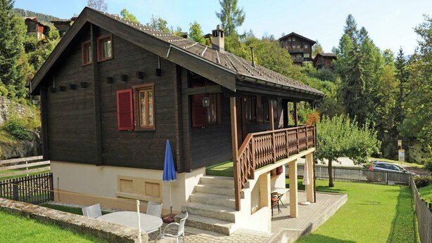 A chalet-style house with a wooden exterior, a balcony, and a small patio area with outdoor seating.