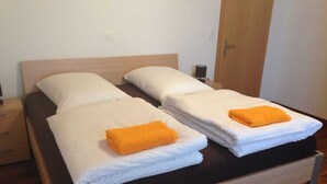 A double bed with white linens and two orange towels.