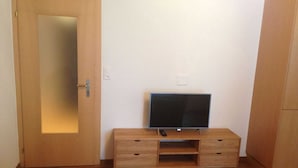 A room with a wooden cabinet, a television on a stand, and a door with a mirror.