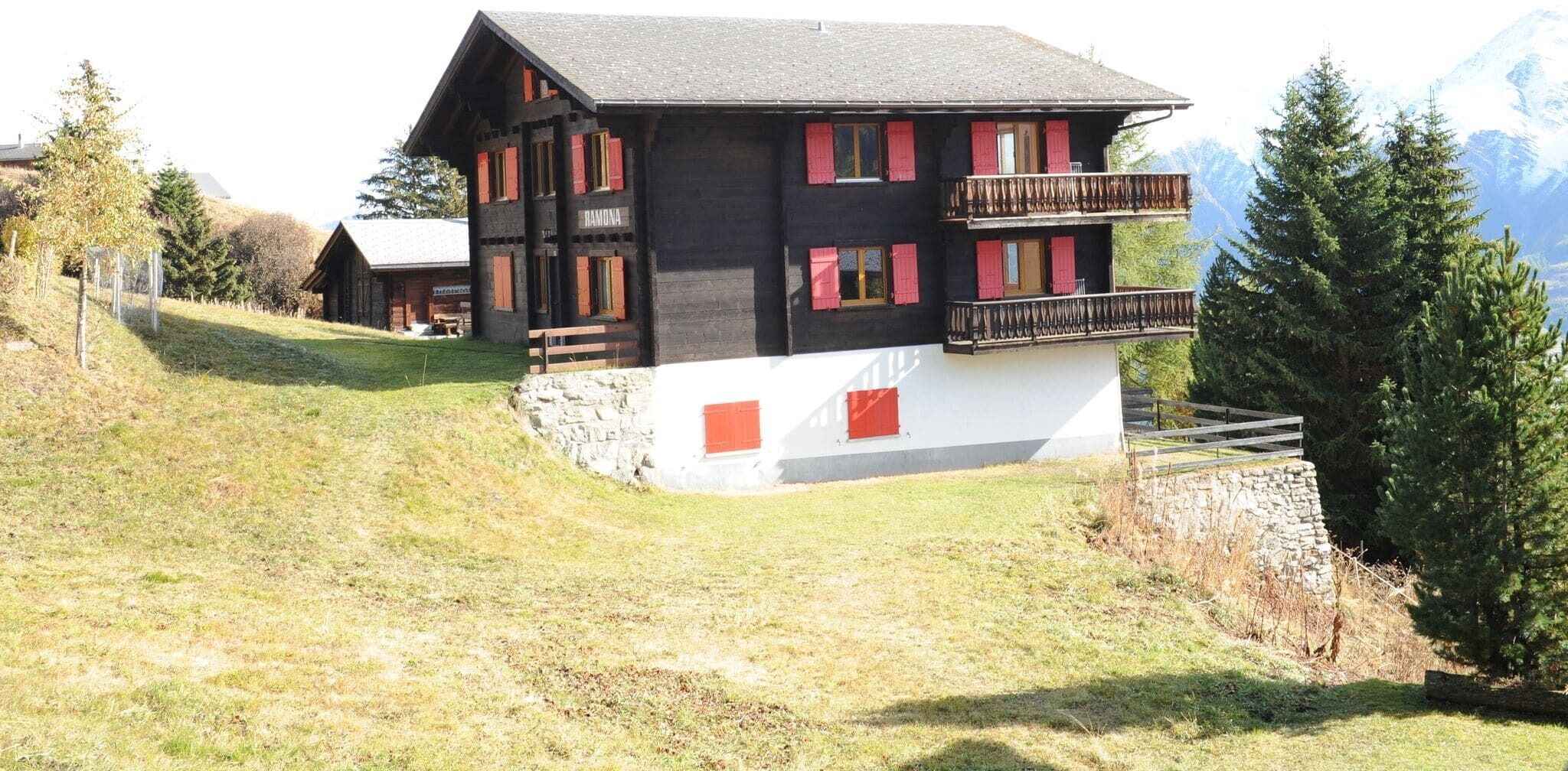 A two-story chalet with a stone foundation, red shutters, and a balcony.