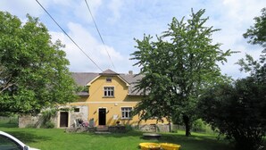 Une maison jaune avec des fondations en pierre, une porte d’entrée et un petit porche avec une chaise.