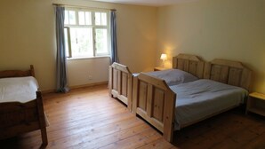 Une pièce avec un lit en bois, une chaise en bois, une fenêtre avec des rideaux et une table de chevet avec une lampe.