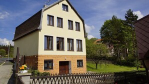 A two-story building with a symmetrical facade, a central entrance, and a small garden area with flowers.