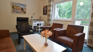 A room with a desk, two chairs, a table with a vase of flowers, and a window with a view of trees. - Serene Holiday Home in Mladé Buky with small pool, Trampoline & Skiing Nearby (Mladé Buky)